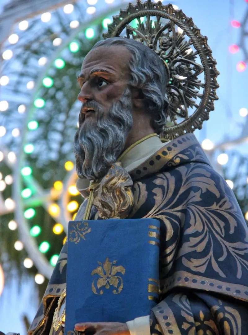 Il volto della statua di Sant’Antonio Abate, con l’aureola d’argento, davanti alle luminarie della festa