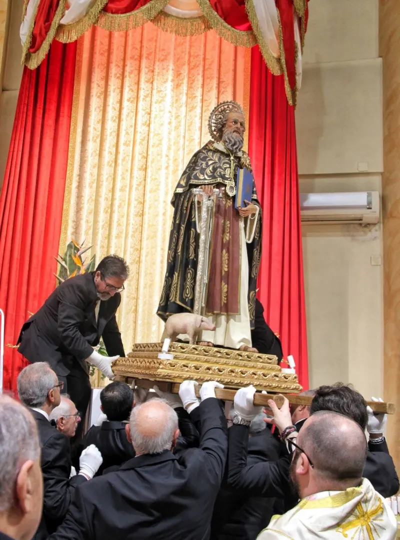I portatori sollevano la statua sulle spalle davanti al drappo rosso dell’altare
